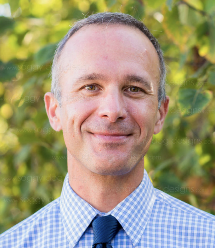 phot of man smiling wearing a tie in front of tree